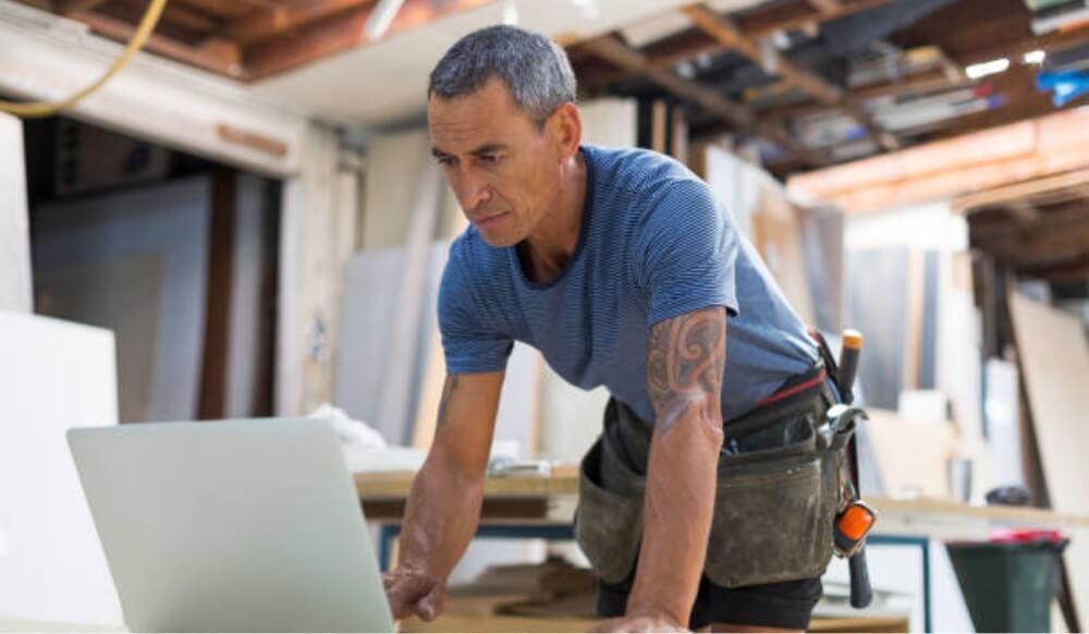 A tradesman leaning over a laptop in a workshop